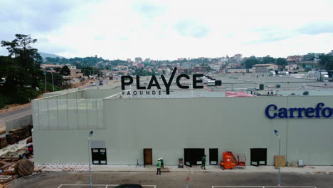 Drone-shot-away-from-the-PlaYce-shopping-mall-logo-in-cloudy-Yaounde,-Cameroon