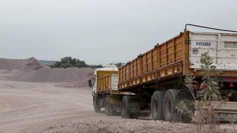 Yellow-dump-truck-driving-through-a-mining-area-with-mounds-of-earth,-overcast-sky,-static-shot