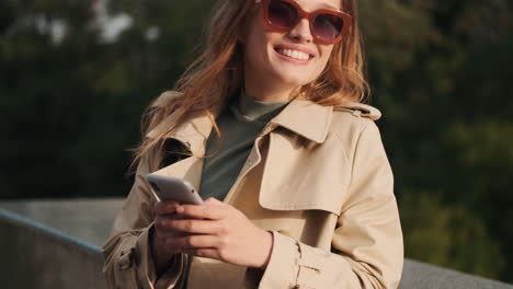 Caucasian-female-student-using-smartphone-and-smiling-outdoors.