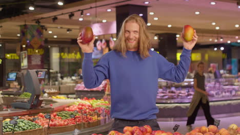 Caucasian-young-man-dancing-with-mangoes-in-hands-while-shopping-in-a-supermarket