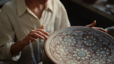 Smiling-ceramist-touching-clay-plate-in-workshop