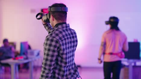 Ein-Junger-Afroamerikanischer-Mann-Mit-Einem-Virtual-Reality-Headset-Dreht-Sich-In-Einem-Konferenzraum-Im-Kongresszentrum-Voller-VR-Gaming-Stationen-Mit-Violettem-Neonlicht-Um