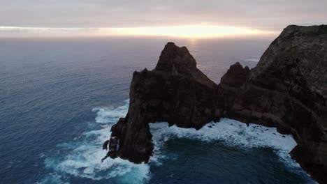 Drone-flying-over-the-blue-ocean-while-viewing-a-cliffside-at-sunset-at-Madeira,-Ponta-Do-Rosto
