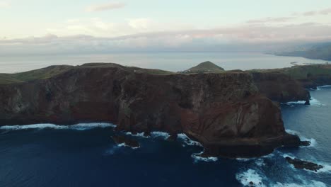 Drone-flying-over-the-sea-by-the-coast-at-Ponta-Do-Rosto,-Madeira-while-scenery-landscape-visible-in-the-background-with-waves-and-mountains-at-Madeira