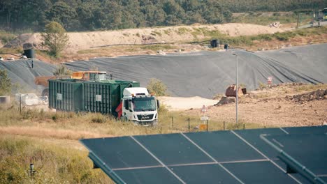 a-semi-trailer-drives-between-solar-panels-and-a-landfill-site