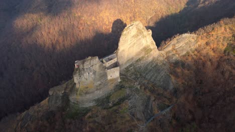 Majestic-ancient-fortress-perched-on-a-steep-cliff-during-autumn,-aerial-view