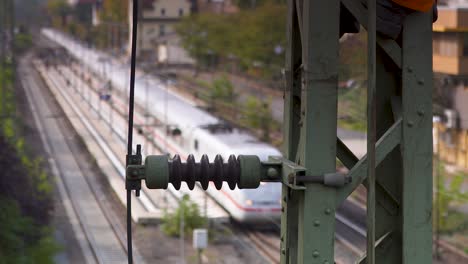 Train-approaching-on-tracks-viewed-through-blurred-industrial-equipment-at-dusk,-evoking-a-sense-of-transit-and-movement