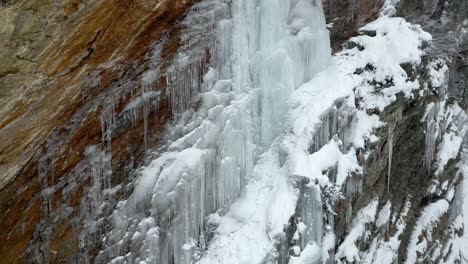 Winter-snow-and-Ice-cascade-formations-on-mountain-rock-face-AERIAL-CRANE