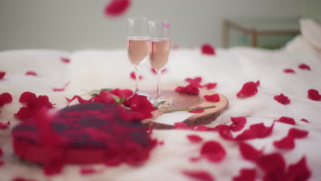 Rose-petals-falling-on-Valentine's-Day-bedroom-setting-with-wine,-slow-motion