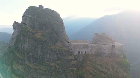 Alte-Festung-Auf-Einer-Klippe-In-Einer-Bergregion,-Umgeben-Von-Sonnenstrahlen,-Luftaufnahme