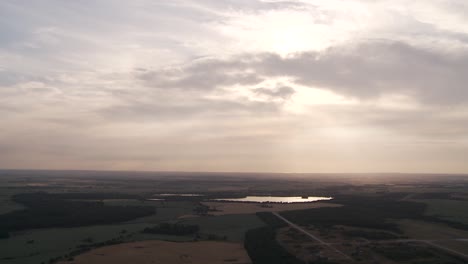 Luftaufnahme-Eines-Ruhigen-Sees-Bei-Sonnenuntergang-Mit-Weitläufigen-Feldern-Unter-Einem-Bewölkten-Himmel