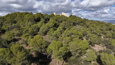 Ascending-drone-shot-showing-Castell-de-Bellver-in-green-landscape-of-Mallorca-during-cloudy-day---backwards-shot