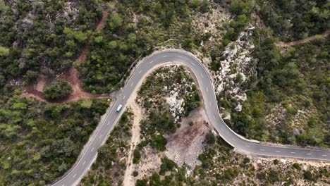 Aerial-top-down-shot-of-car-driving-on-curvy-road-in-Esporles-during-sunny-day,-Mallorca