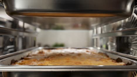 Close-up-of-a-professional-kitchen's-steel-oven-with-a-lasagna-dish-in-focus,-creating-a-warm,-busy-atmosphere