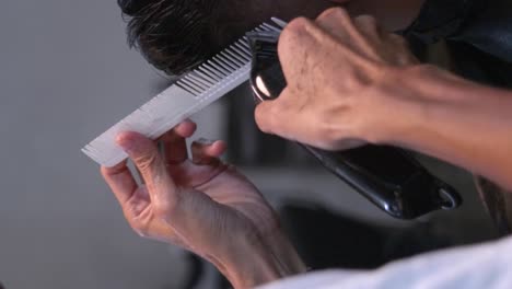 White-comb-and-battery-powered-hair-clipper-used-to-trim-and-level-edges-of-black-hair-on-rear-right-of-head,-filmed-in-closeup-shot-in-vertical-handheld-slow-motion-style