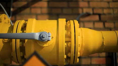 Close-up-of-a-bright-yellow-gas-pipeline-with-flanges,-set-against-a-brick-wall,-highlighting-industrial-infrastructure