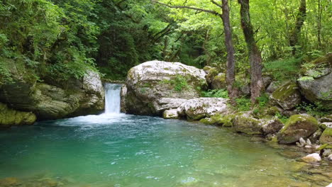 Bathed-in-the-sun's-magical-glow,-a-waterfall-cascades-down-the-river,-surrounded-by-green-forest-trees-and-lush-greenery,-creating-an-enchanting-natural-scene-in-Kouiassa-waterfall,-Epirus