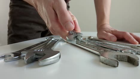 Man-choosing-small-adjustable-wrench,-multiple-spanners-on-worktop