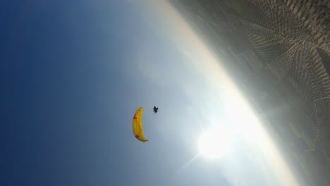 Vertical-format:-Aerial-orbits-below-motor-paraglider-in-blue-sky