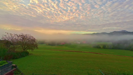Thin-mist-rolling-over-rural-countryside-below-sunset-sky,-timelapse