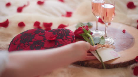 Die-Hände-Einer-Frau-Legen-Eine-Valentinstagskarte-Und-Eine-Rose-Auf-Eine-Holzplatte