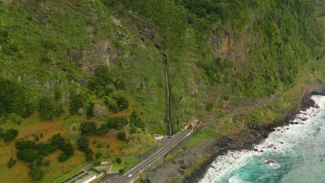 Aerial-top-down-shot-of-waterfall-with-driving-car-on-coastal-road-on-Madeira-Island