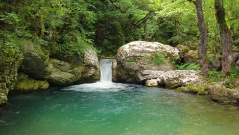 The-enchanting-scene-unfolds-as-the-sun's-magical-glow-illuminates-the-river-in-Kouiassa-waterfall,-Epirus,-where-a-waterfall-cascades-amidst-the-beauty-of-green-forest-trees-and-luxuriant-greenery