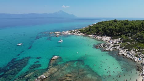 Menschen-Schwimmen-Im-Klaren-Blauen-Meer-An-Der-Orangefarbenen-Strandbucht-In-Chalkidiki,-Griechenland---Luftbild-4k