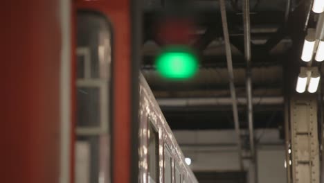 Train-at-a-station-with-red-and-green-signal-lights-in-focus,-industrial-setting