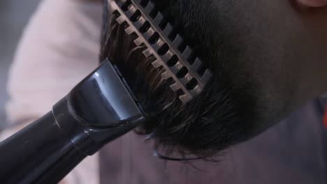 Black-brush-comb-and-black-hair-dryer-used-to-comb-straighten-black-hair-on-top-of-black-head-by-barber,-filmed-in-closeup-shot-in-vertical-handheld-slow-motion-style