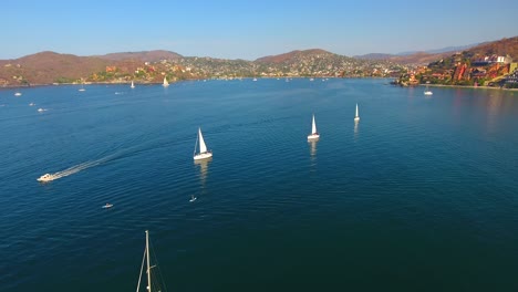 Flying-down-over-sailboats-racing-around-a-calm-water-bay-off-the-coast-of-Zihuatanejo,-Mexico