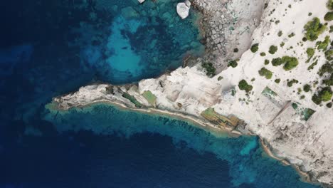 Die-Drohne-Fliegt-Von-Oben-Nach-Unten-über-Einer-Kleinen-Felsigen-Küste-Mit-Dem-Klaren-Blauen-Meer-Auf-Ibiza,-Spanien.-Luftaufnahmen-In-4K