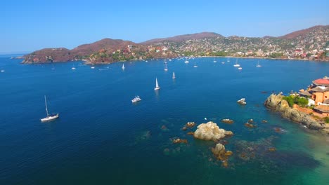 Stationary-aerial-view-of-a-busy-ocean-bay-filled-with-sailboats-and-yachts-off-the-coast-of-Zihuatanejo,-Mexico