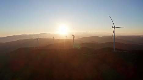 Sunset-rays-between-wind-turbines-spinning-on-mountains,-green-energy