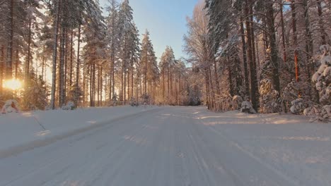 Winter-driving-POV-on-snow-covered-forest-roads-highlighted-by-sun-rays