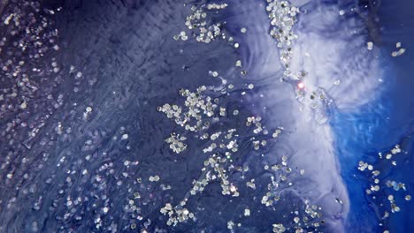 Macro-shot-of-blue-ink-dispersing-in-water-with-white-particles,-resembling-a-cosmic-galaxy