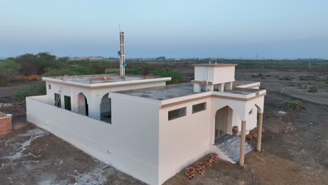 Aerial-profile-view-of-newly-constructed-mosque-with-loudspeakers-installed-on-the-tower-during-daytime-in-a-village-near-Nawabshah,-Sindh-,-Pakistan