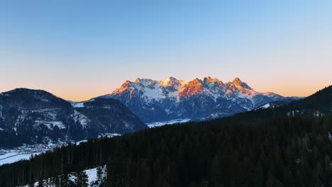 The-drone-is-flying-over-a-mountain-with-trees-revealing-a-big-mountain-lit-by-the-golden-sun-during-sunset-in-Austria-Aerial-Footage-4K