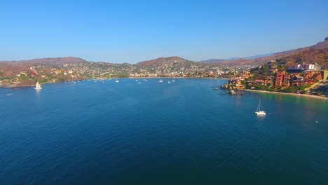 Drone-flying-high-above-a-still-water-bay-with-many-boats-anchored-off-the-shore-of-a-quiet-town-on-the-western-coast-of-Mexico
