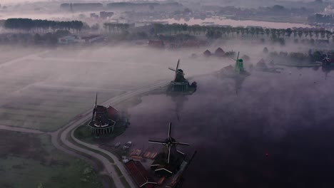 Die-Drohne-Fliegt-über-Den-Windmühlen-Der-Zaanse-Schans-Mit-Viel-Nebel-Bei-Sonnenaufgang-In-Den-Niederlanden.-Luftaufnahmen-In-4K