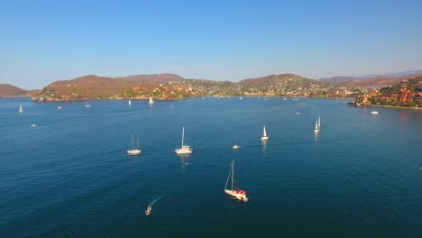 Panning-over-a-bay-filled-with-a-regatta-of-sailing-vessels-and-yachts-offshore-from-Zihuatanejo,-Mexico