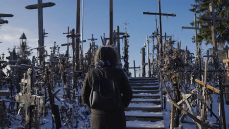 Pilgrim-woman-wearing-coats-walks-uphill-on-the-Hill-of-Crosses-in-Lithuania