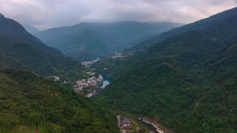 Drone-shot-of-river-and-village-in-valley-between-greened-mountains-of-Wulai-烏來區,-Taiwan---Wide-shot