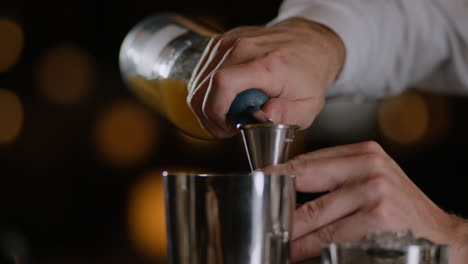 Closeup-shot-of-a-bartender-measuring-liquor-into-a-jigger-and-pouring-it-into-a-metal-shaker