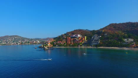 Aerial-video-flying-by-the-gorgeous-shoreline-filled-with-boats,-white-sand-beaches,-and-the-beautiful-city-of-Zihuatanejo,-Mexico