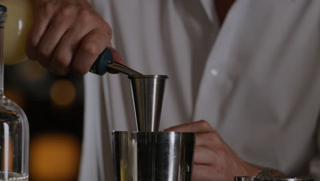 Closeup-shot-of-a-bartender-measuring-liquor-into-a-jigger-and-pouring-it-into-a-metal-shaker