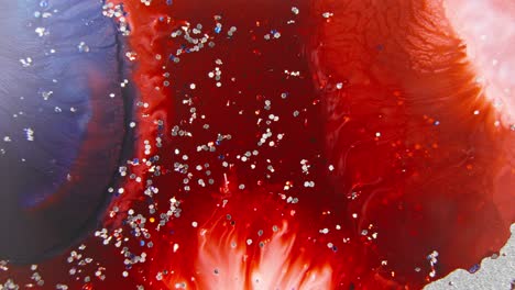 Red-and-navy-blue-ink-mixing-in-water-with-sparkling-glitter,-creating-a-cosmic-nebula-effect