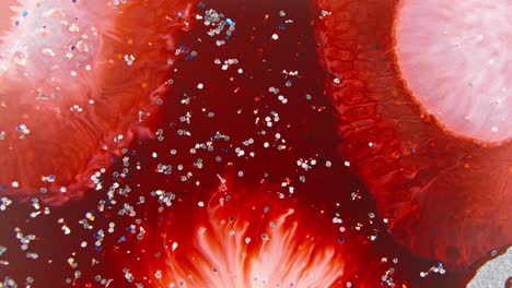 Bright-red-ink-expanding-in-water-with-sparkling-particles,-creating-an-intense-and-abstract-visual-effect