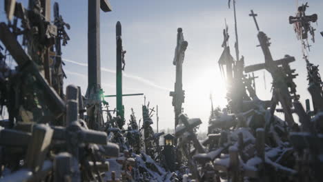many-crosses-accumulated-and-piled-up,-ancient-religious-crosses-with-rosaries-in-a-counter-light-with-the-sun's-rays,-under-a-blue-sky,-in-winter,-cinematic-shot-in-slow-motion