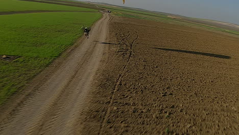 Aerial-swoops-down-to-paramotor-glider-skimming-rural-gravel-road
